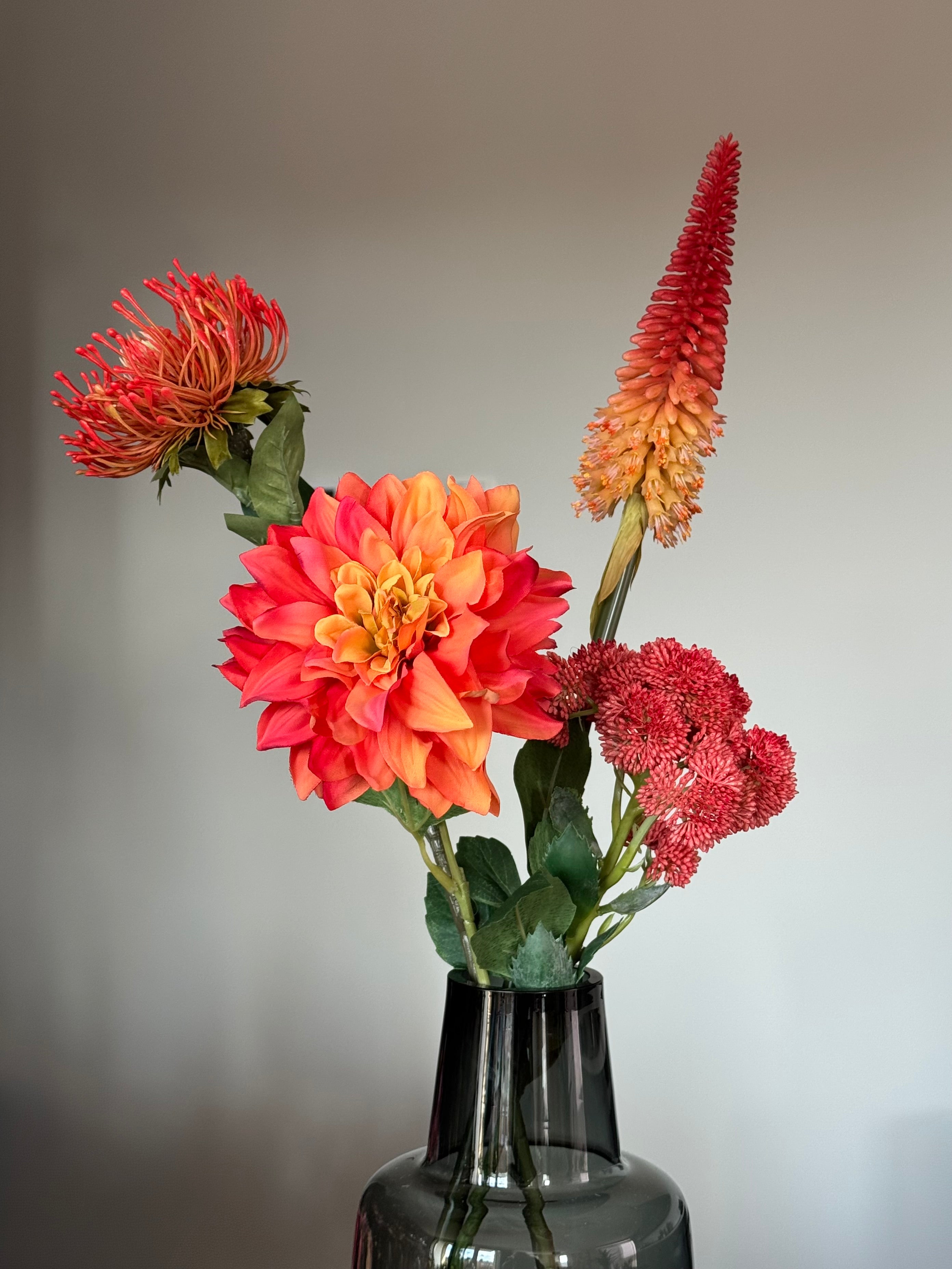 Design kunstboeket in rood met zwart doorschijnende vaas close up