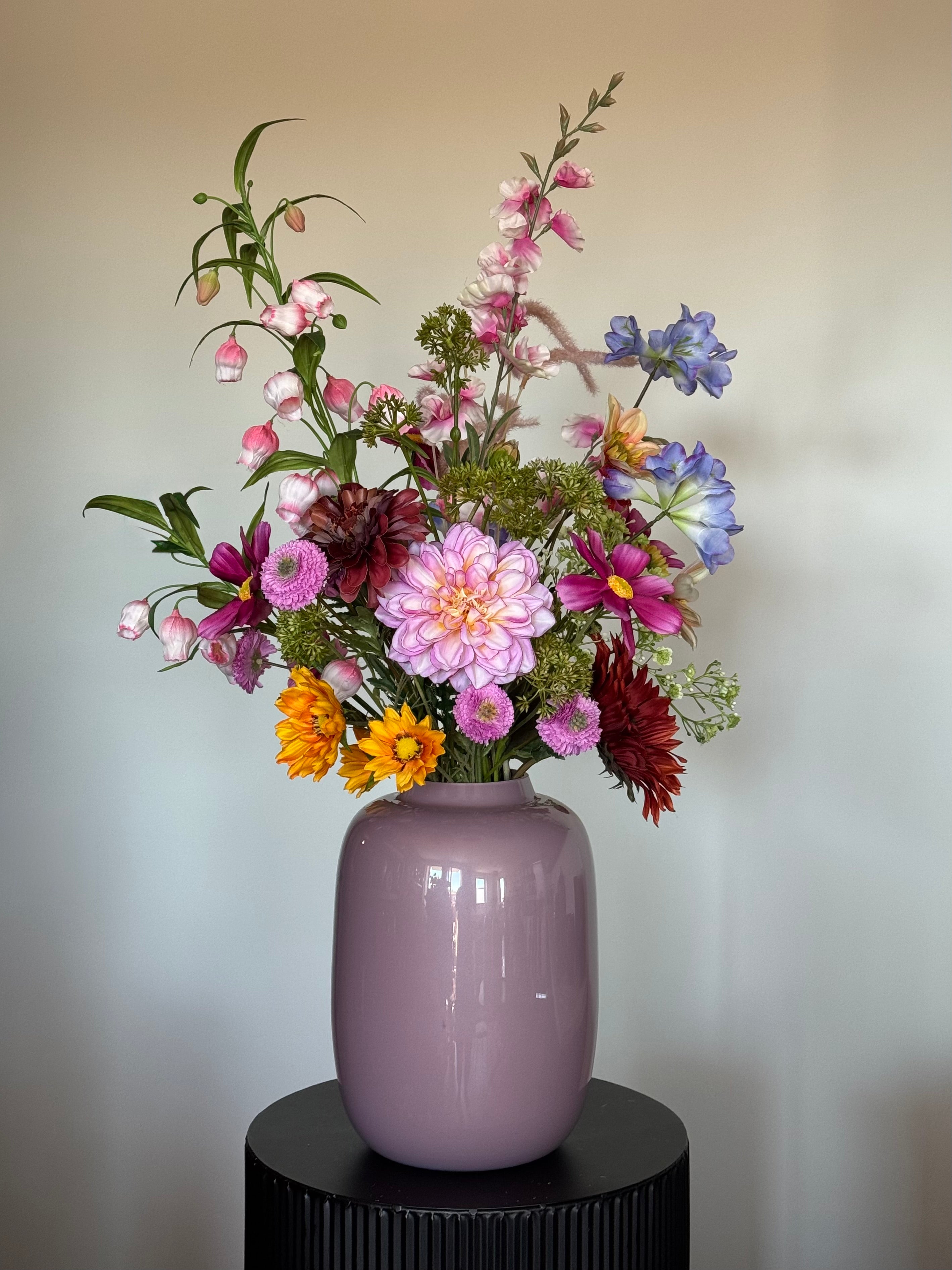 Zijden veldboeket met bonte bloemen en bijpassende vaas op een sokkel.