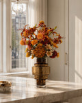 Warm oranje zijden boeket met chrysanten, lelies en zonnehoedbloemen op een marmeren kookeiland in een luxe interieur.